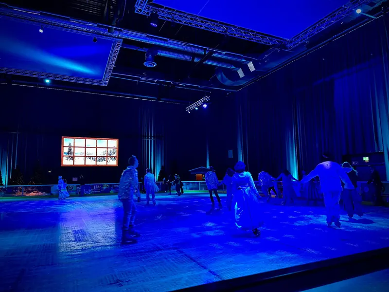 The blue-lit indoor ice rink at Metropolis Halle Potsdam with skaters
